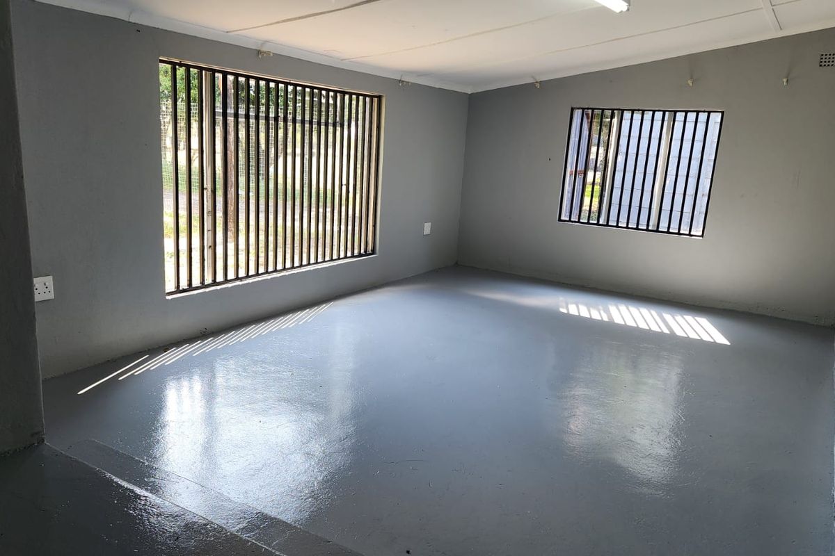 An empty living area featuring painted concrete flooring, grey walls, and windows fitted with security bars.