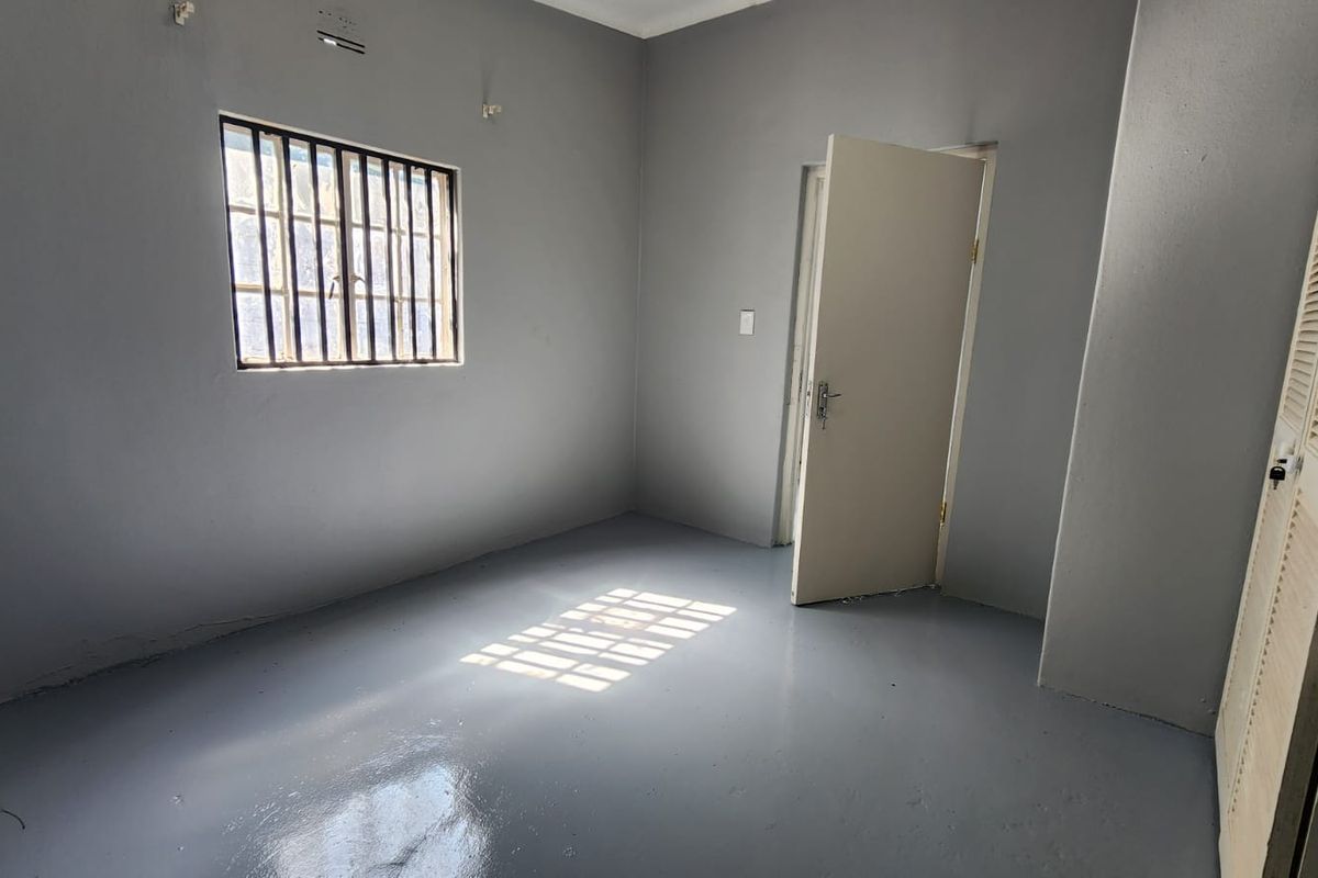 An empty bedroom featuring painted concrete flooring, a window with security bars, and a built-in cupboard.
