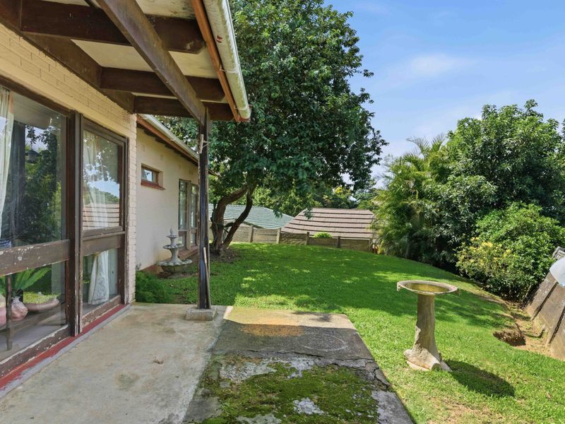 A covered concrete patio overlooking a private garden, featuring timber roof beams and direct access to the home via sliding glass doors.