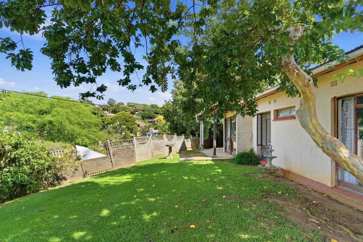 Rear view of the property featuring a lawned garden, paved patio area, and precast concrete boundary wall.