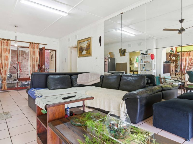 Spacious living area featuring tiled flooring, a large mirrored wall, and a ceiling fan, offering a functional layout with potential for modernization.