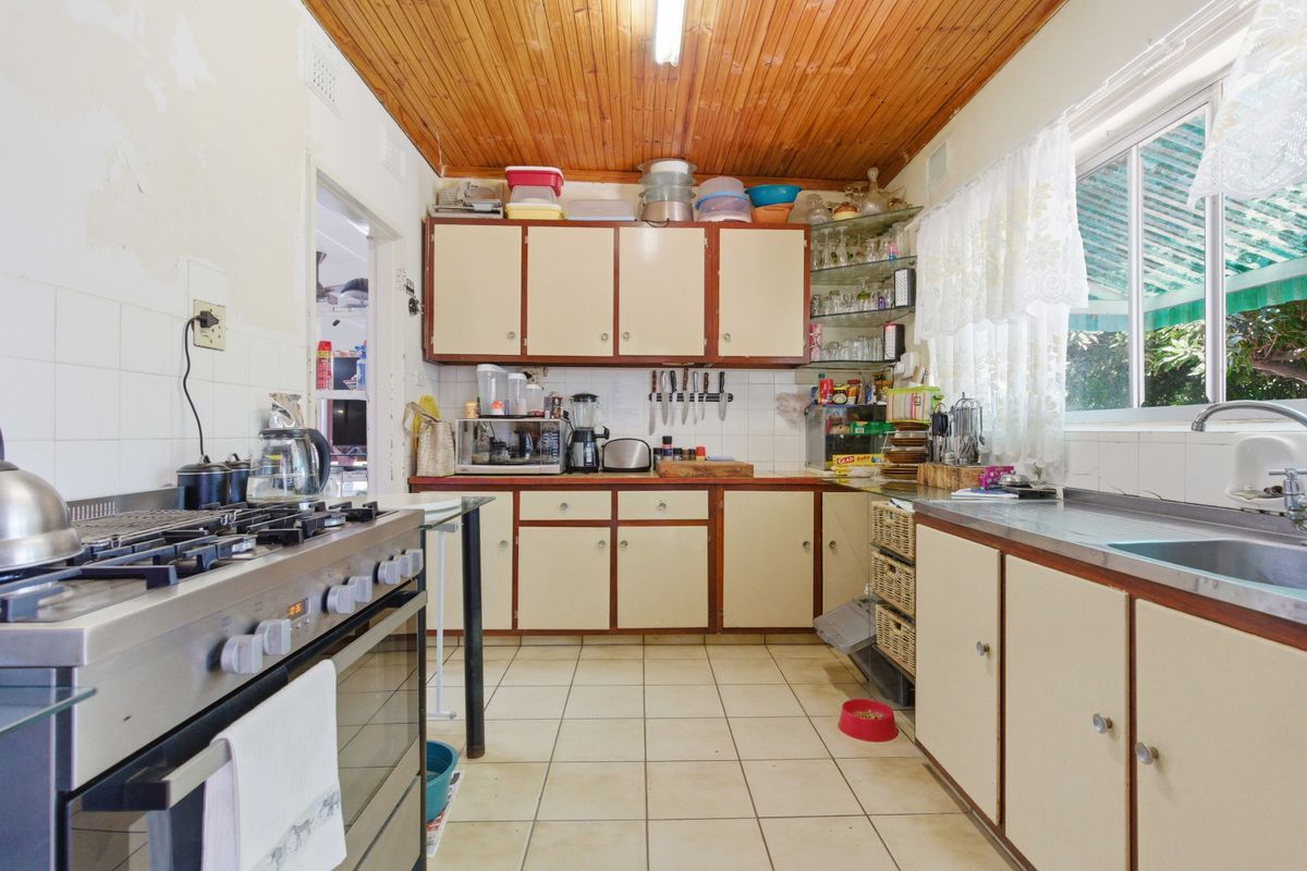 A dated kitchen featuring timber ceilings, tiled flooring, built-in cabinetry, and a gas stove, offering significant potential for modernization and renovation.