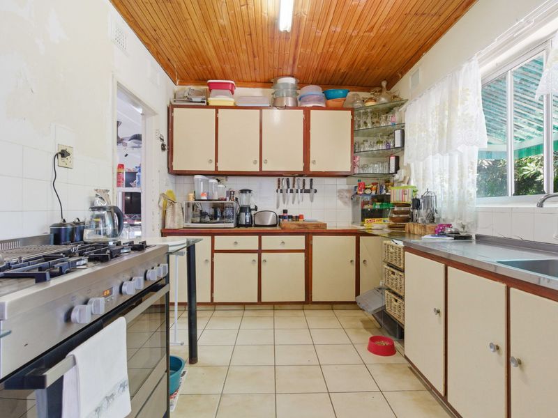 A dated kitchen featuring timber ceilings, tiled flooring, built-in cabinetry, and a gas stove, offering significant potential for modernization and renovation.