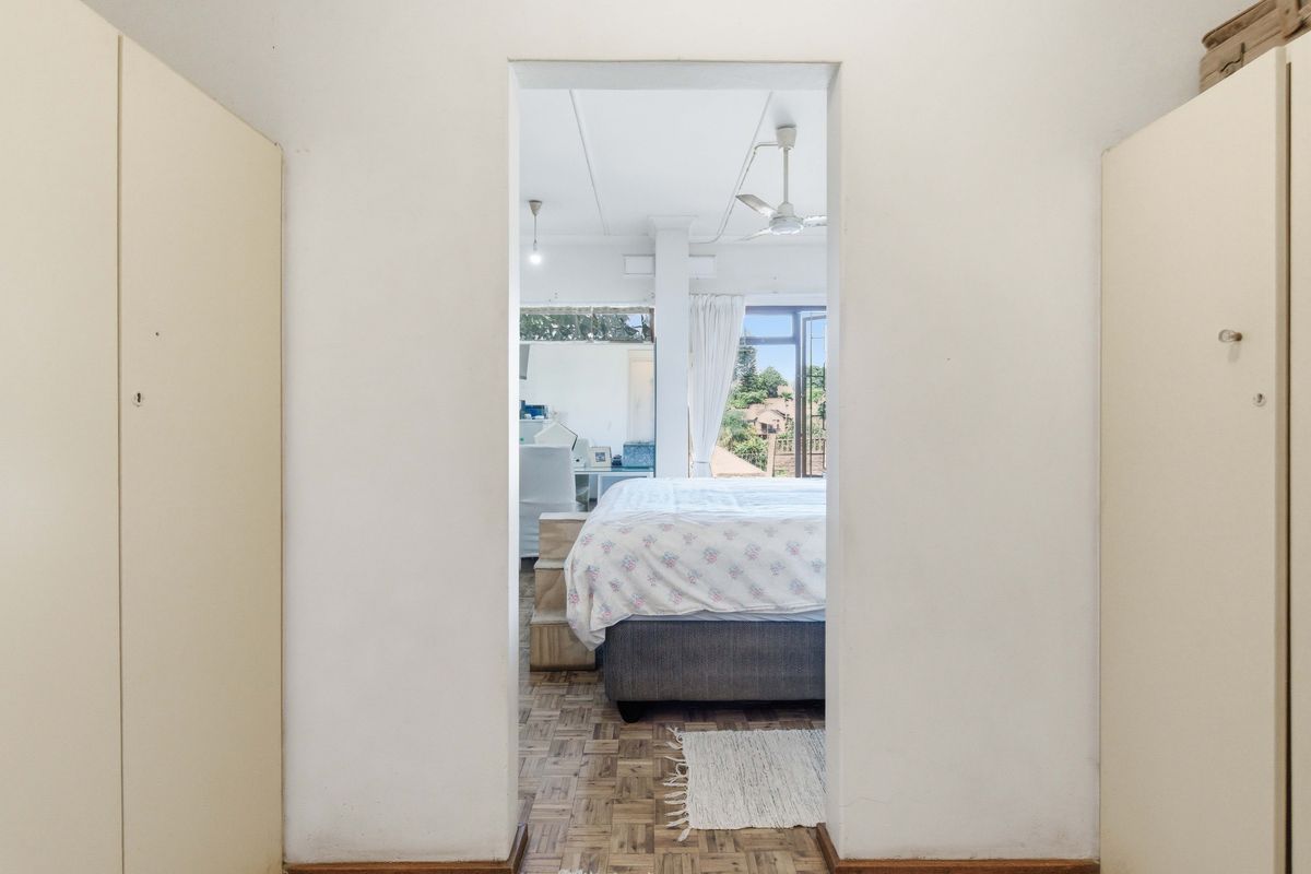A view through a doorway into a bedroom featuring parquet flooring, built-in cupboards, and a ceiling fan with access to an outdoor area.