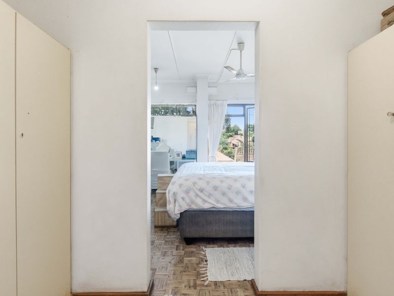 A view through a doorway into a bedroom featuring parquet flooring, built-in cupboards, and a ceiling fan with access to an outdoor area.