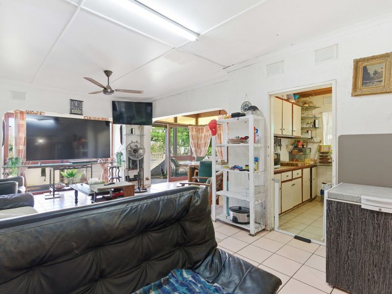 Open plan living area featuring tiled flooring, ceiling fan, and direct access to a rear patio, with an adjacent dated kitchen space.