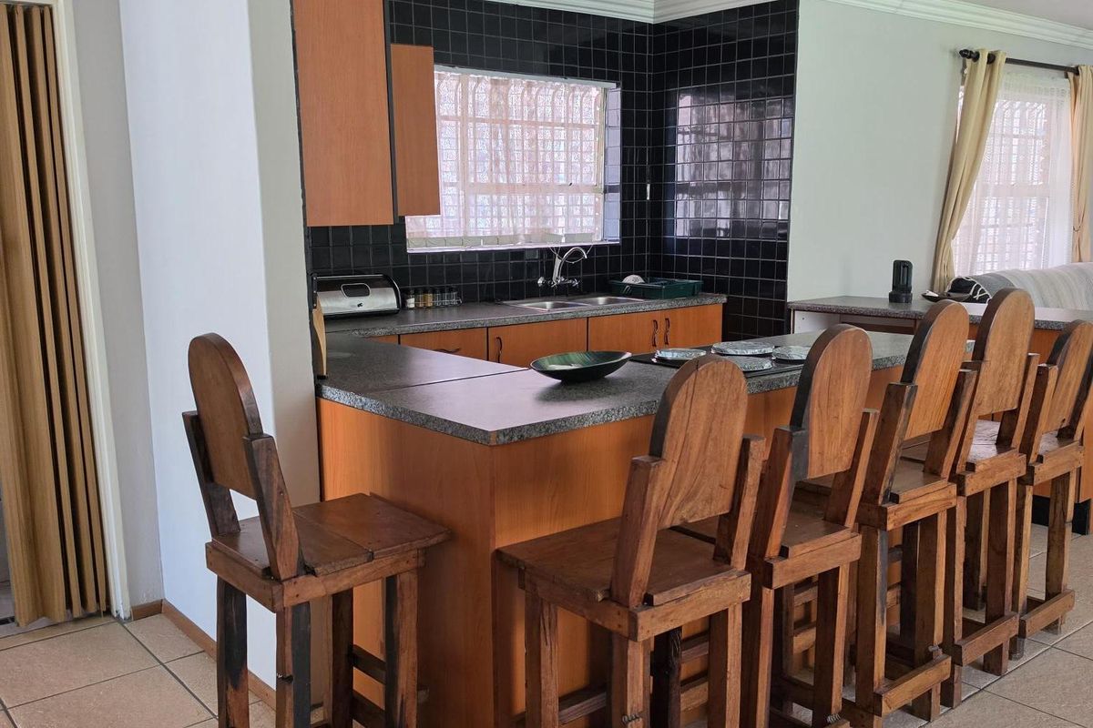 A functional kitchen featuring laminate cabinetry, a breakfast bar, double basin sink, and dark tiled splashbacks, finished with ceramic floor tiles and crown molding.