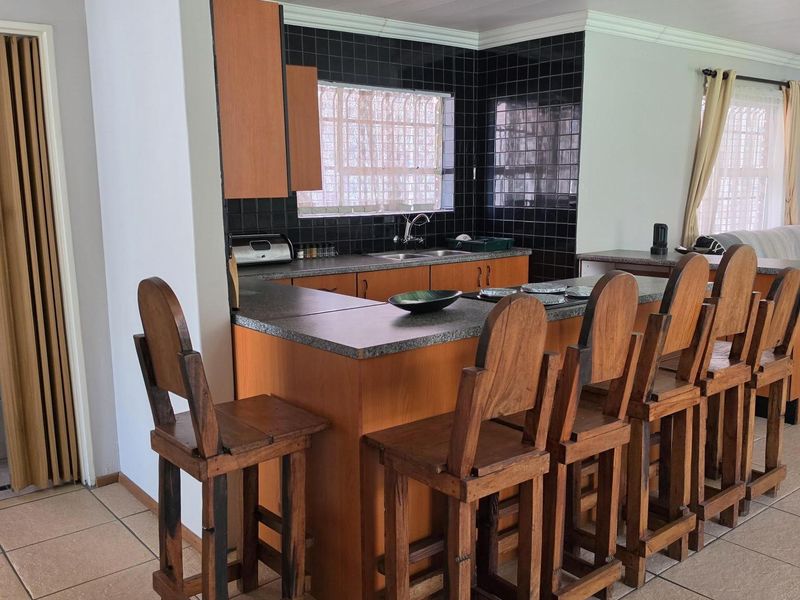 A functional kitchen featuring laminate cabinetry, a breakfast bar, double basin sink, and dark tiled splashbacks, finished with ceramic floor tiles and crown molding.