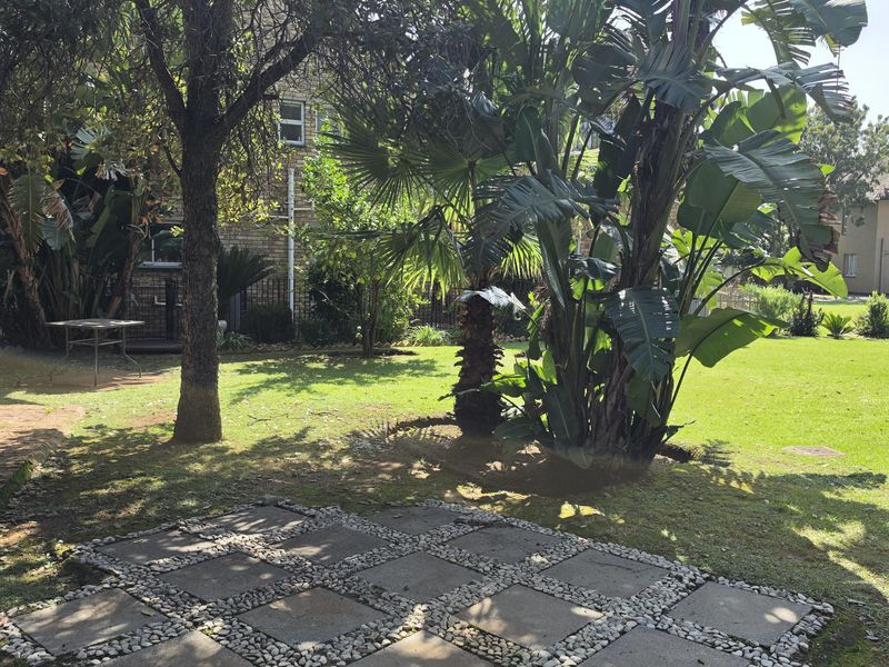 A spacious garden featuring a paved stone patio area, mature trees, and established landscaping, providing a private outdoor space.