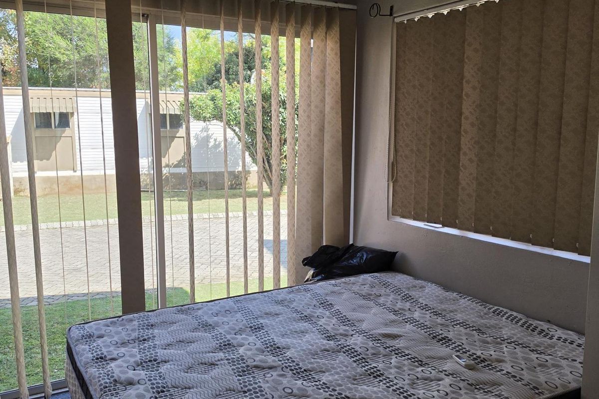 A bedroom featuring carpet flooring, a wall-mounted split-system air conditioner, and large sliding glass doors with vertical blinds providing access to the exterior.