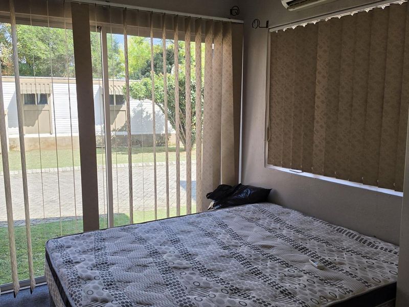 A bedroom featuring carpet flooring, a wall-mounted split-system air conditioner, and large sliding glass doors with vertical blinds providing access to the exterior.