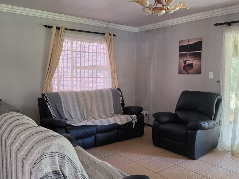A living room featuring ceramic floor tiles, decorative ceiling cornicing, and a window fitted with security bars.