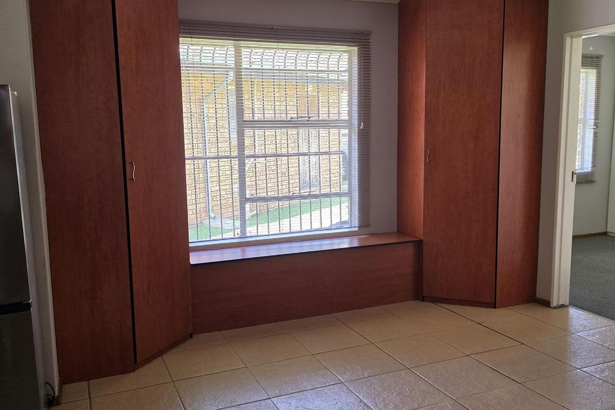 An empty living area featuring tiled flooring, built-in wooden cupboards flanking a window with security bars, and a simple ceiling light fixture.