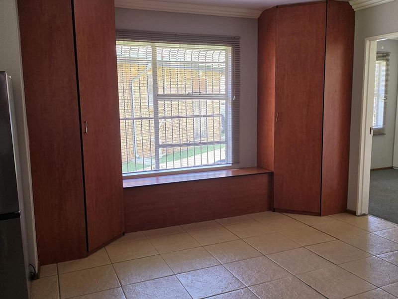 An empty living area featuring tiled flooring, built-in wooden cupboards flanking a window with security bars, and a simple ceiling light fixture.