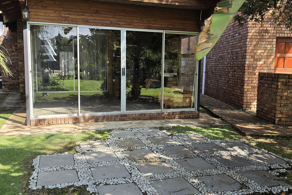 Rear view of the property featuring a timber-clad structure with large sliding glass doors and a paved patio area set within the garden.