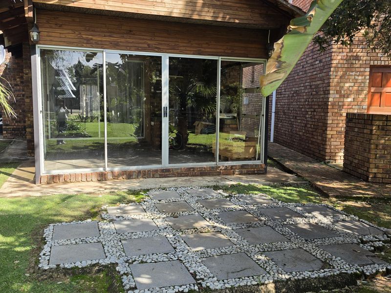 Rear view of the property featuring a timber-clad structure with large sliding glass doors and a paved patio area set within the garden.
