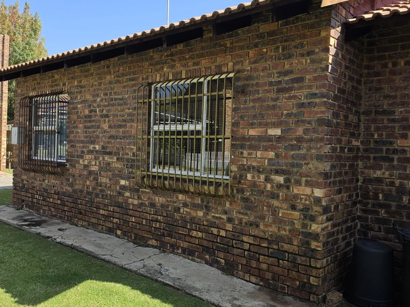 Rear exterior view of the face brick house featuring security bars on windows and a surrounding lawn area.