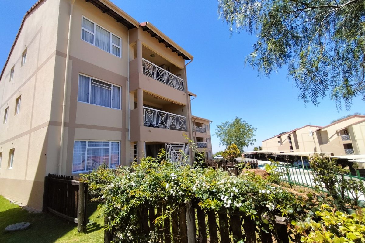 A view of the rear elevation of a multi-story townhouse complex featuring private balconies with metal railings and a well-maintained garden area.