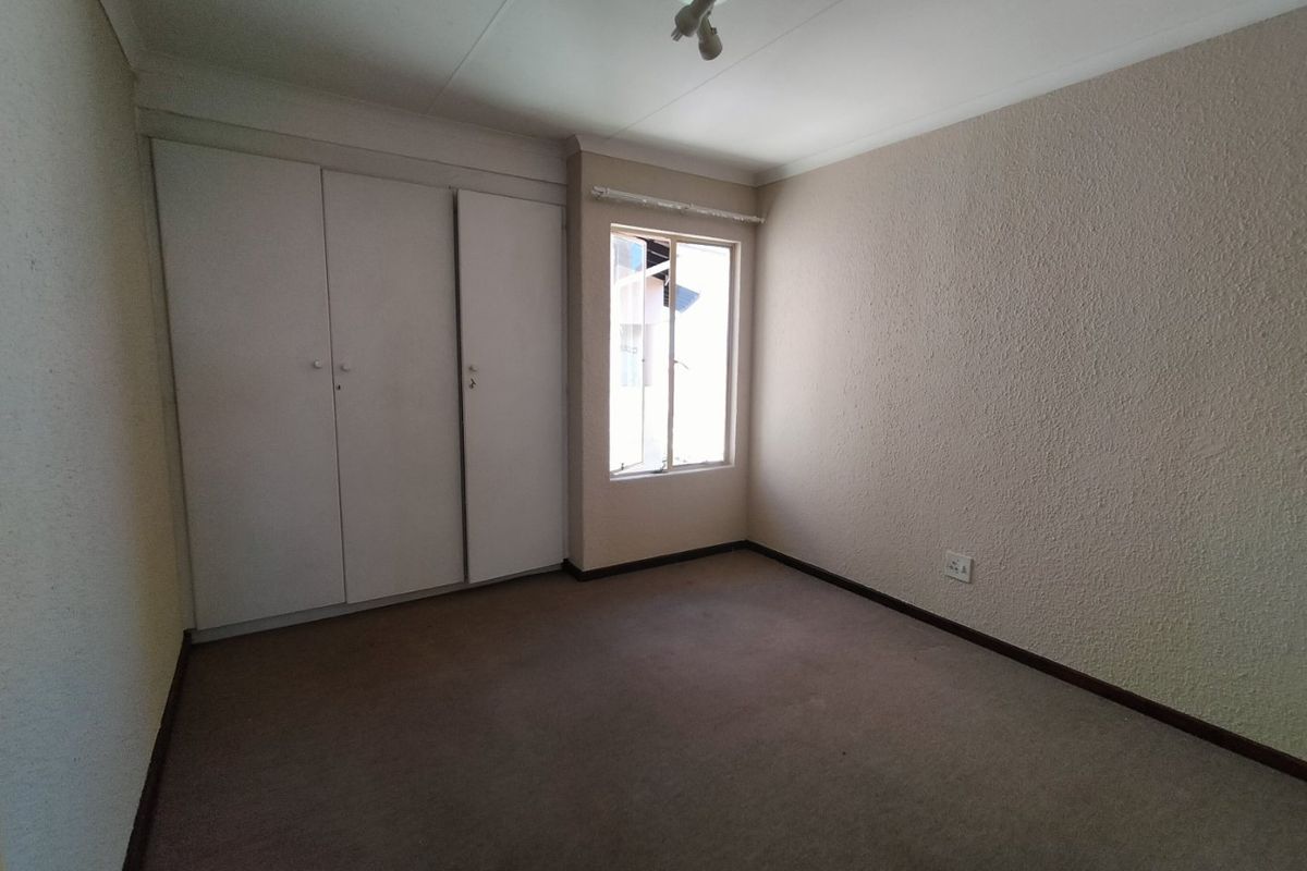 A vacant bedroom featuring built-in cupboards, carpeted flooring, and a window, providing a neutral space ready for personalization.