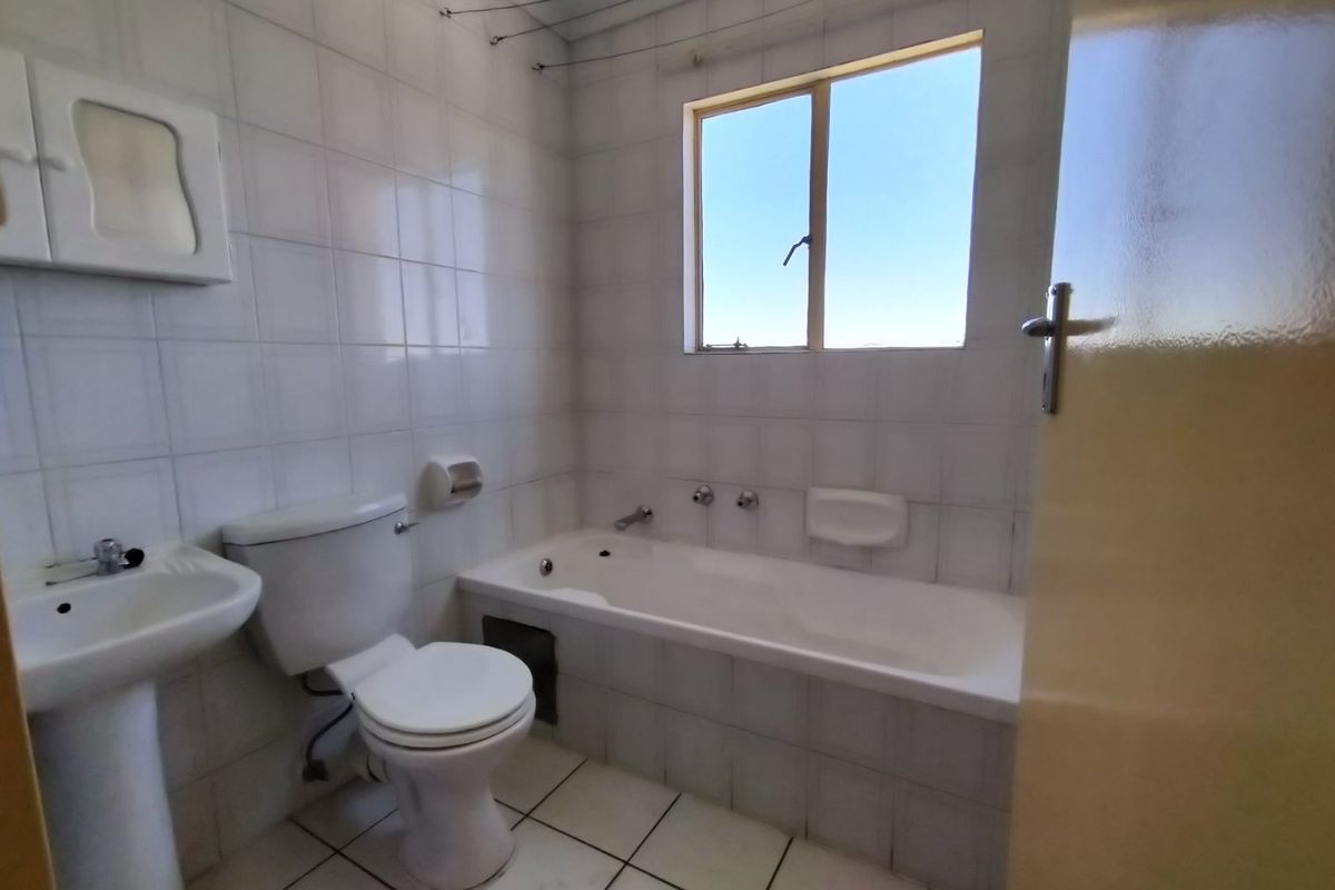 A functional bathroom featuring a pedestal basin, toilet, and built-in bathtub with full-height wall tiling and tiled flooring.