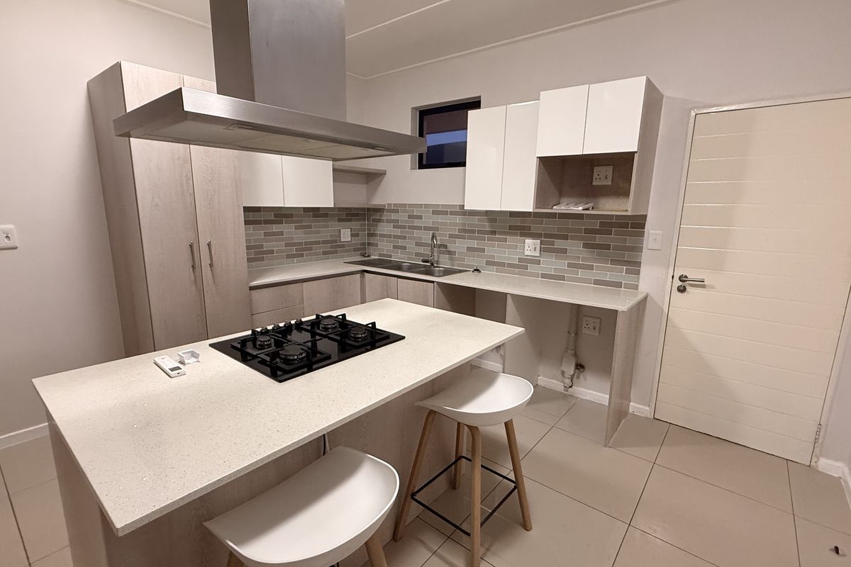 Modern kitchen featuring stone countertops, built-in cabinetry, a gas hob with extractor fan, and a tiled backsplash.