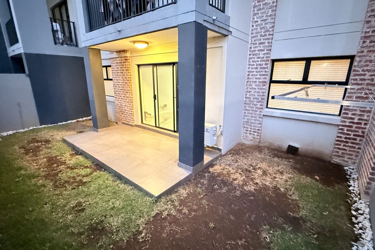 Rear view of the apartment featuring a tiled patio, sliding glass doors, and a small private garden area with exposed brick detailing.