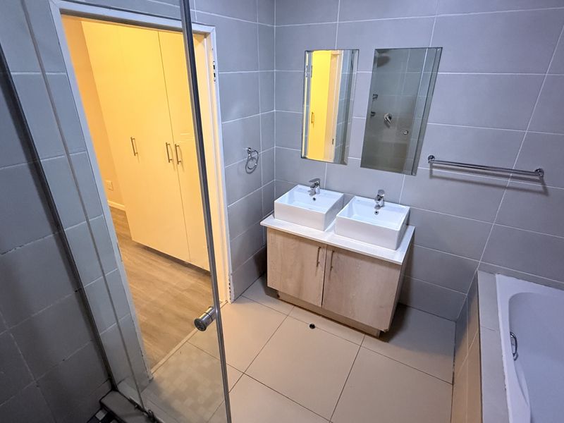 Modern bathroom featuring a double vanity with vessel sinks, tiled walls and flooring, a bathtub, and a separate glass-enclosed shower area.