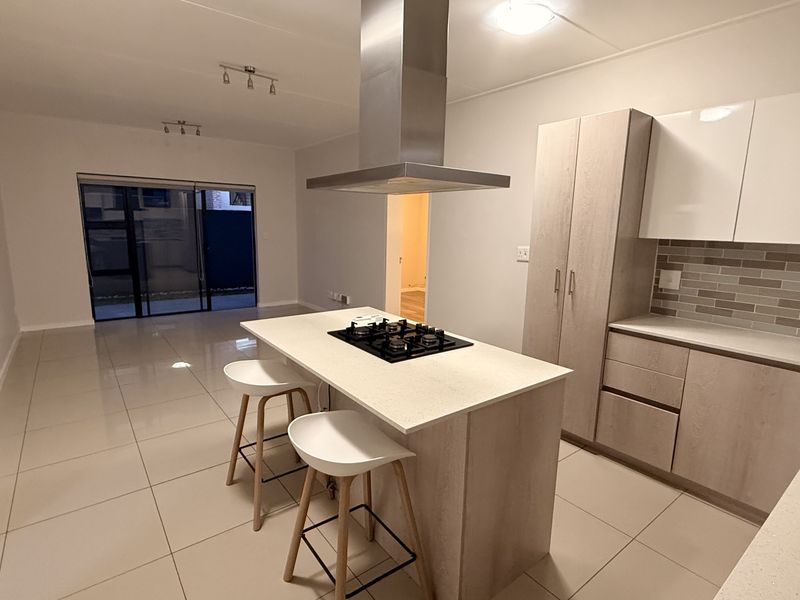 Modern open-plan kitchen and living area featuring a central island with a gas hob, sleek cabinetry, and large sliding doors leading to the exterior.