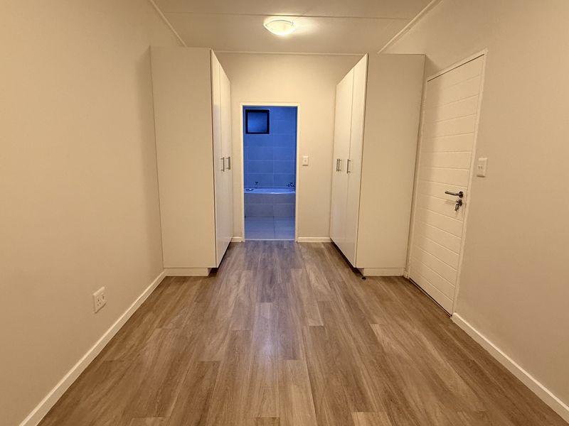 A clean, empty bedroom featuring modern laminate flooring, built-in cupboards, and direct access to an en-suite bathroom.