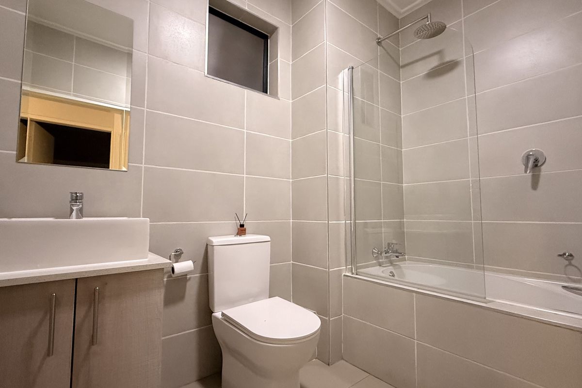 Modern bathroom featuring neutral wall tiles, a vessel sink vanity, a toilet, and a bathtub with a glass shower screen.
