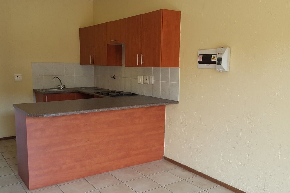 A functional kitchen featuring laminate cabinetry, a gas hob, tiled backsplash, and ceramic floor tiles, presented in a clean, empty state.