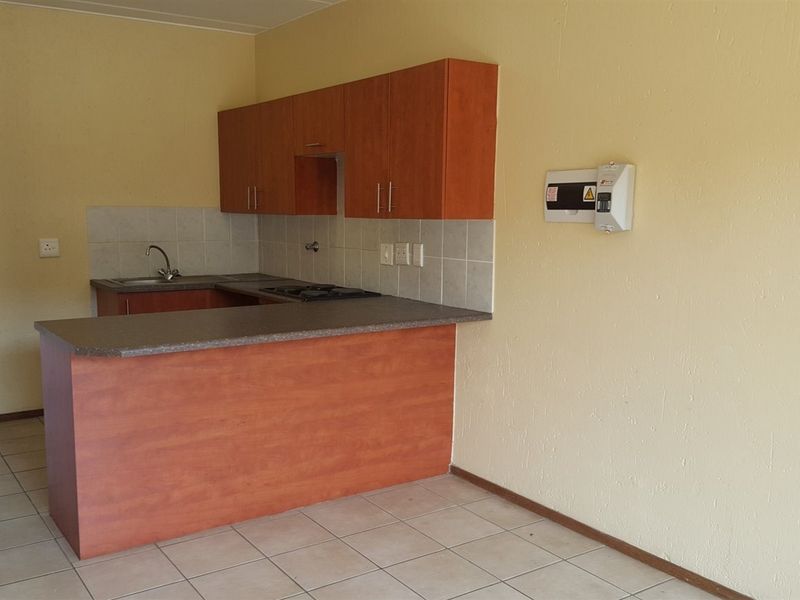 A functional kitchen featuring laminate cabinetry, a gas hob, tiled backsplash, and ceramic floor tiles, presented in a clean, empty state.