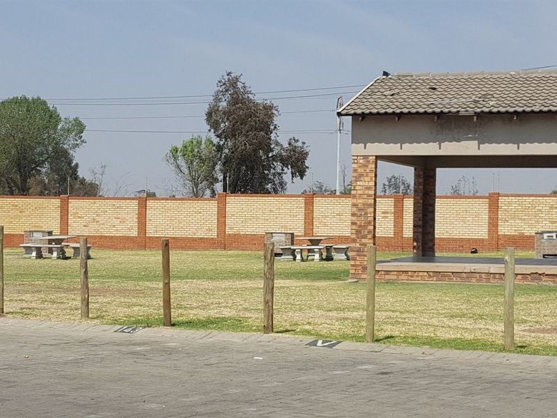 Communal outdoor area featuring a covered patio, brick boundary wall, and paved parking space within a townhouse complex.