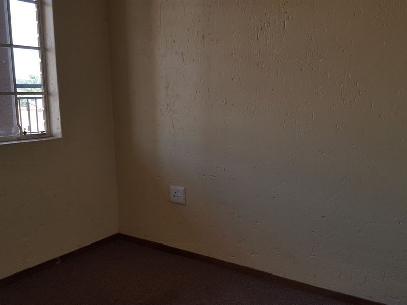 An empty bedroom featuring carpeted flooring, a window with security bars, and a standard electrical wall socket.