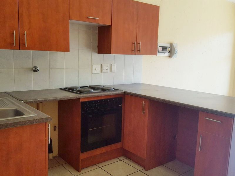 A compact kitchen featuring wood-look cabinetry, laminate countertops, a built-in oven with electric hob, and tiled flooring, currently in need of minor repairs.