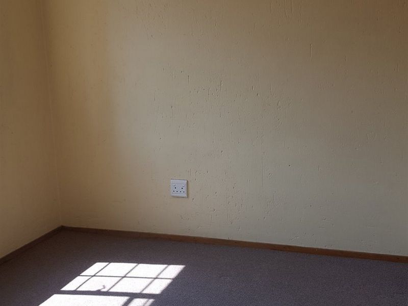 An empty bedroom featuring carpeted flooring, neutral wall paint, and a single electrical wall socket.