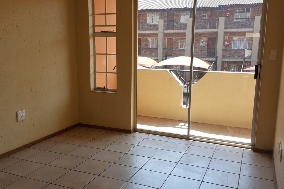 An empty living area featuring tiled flooring, a sliding glass door leading to a balcony, and a side window, awaiting personal touches.