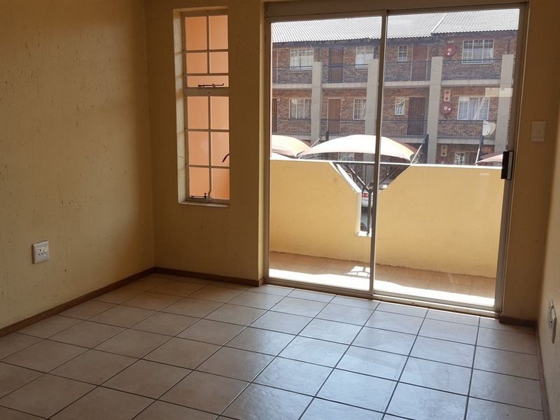 An empty living area featuring tiled flooring, a sliding glass door leading to a balcony, and a side window, awaiting personal touches.