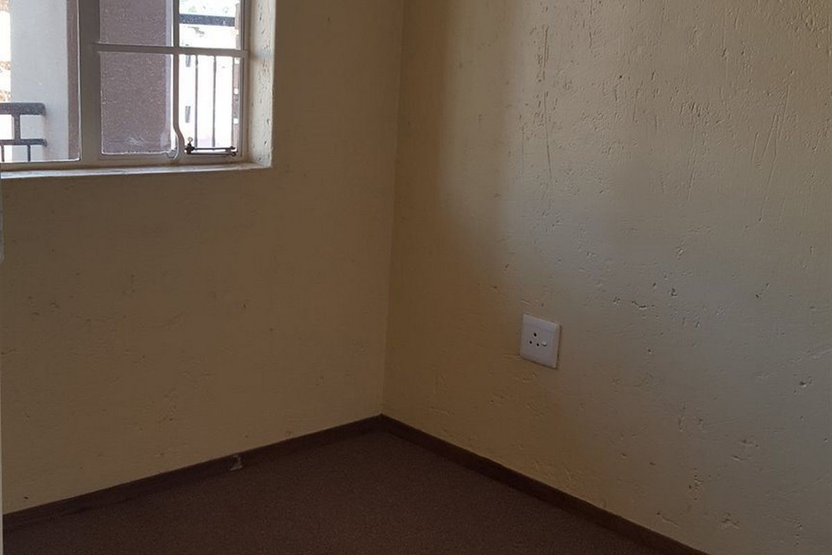 An empty bedroom featuring a steel-framed window, carpeted flooring, and standard electrical outlets, requiring cosmetic updates to improve its overall condition.