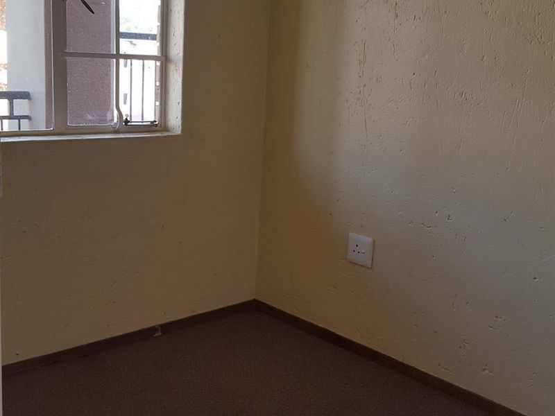 An empty bedroom featuring a steel-framed window, carpeted flooring, and standard electrical outlets, requiring cosmetic updates to improve its overall condition.