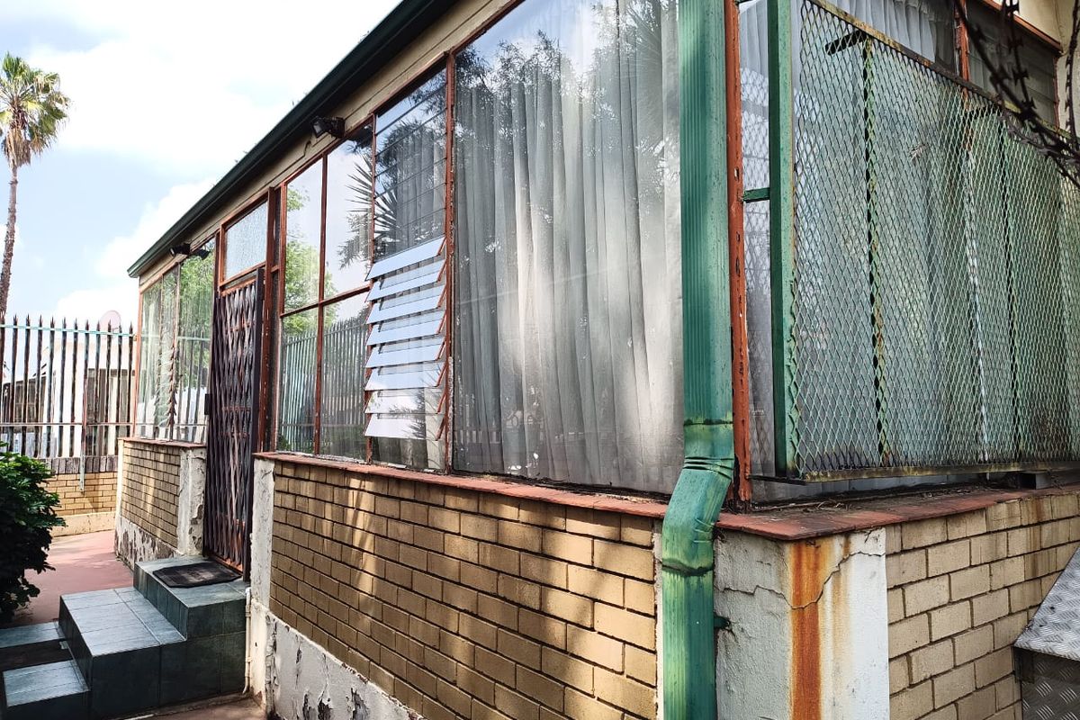 Exterior view of the rear facade featuring brickwork, metal security screening, and tiled steps, showing signs of significant weathering and maintenance requirements.