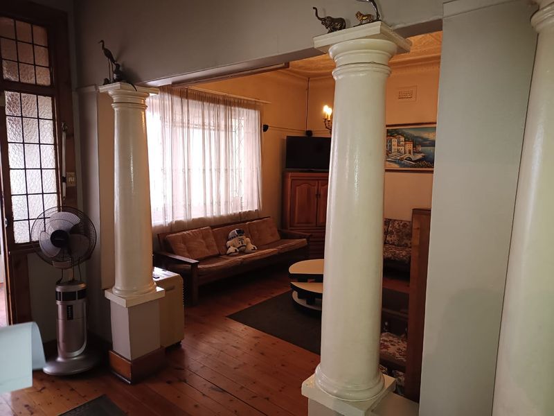 A living room featuring classic decorative columns, original hardwood flooring, and ornate ceiling detailing, offering a traditional architectural aesthetic.