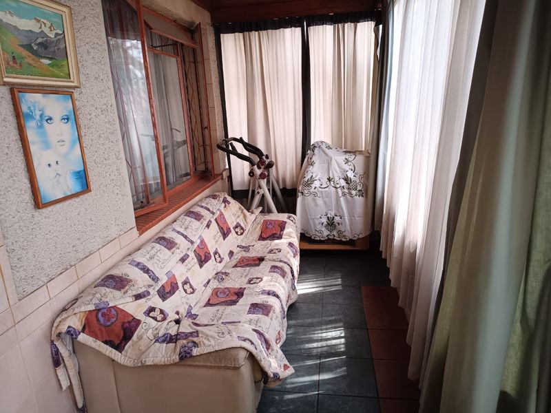 A sun-filled enclosed patio or sunroom featuring tiled flooring and large windows, offering a versatile space for relaxation or a home gym area.