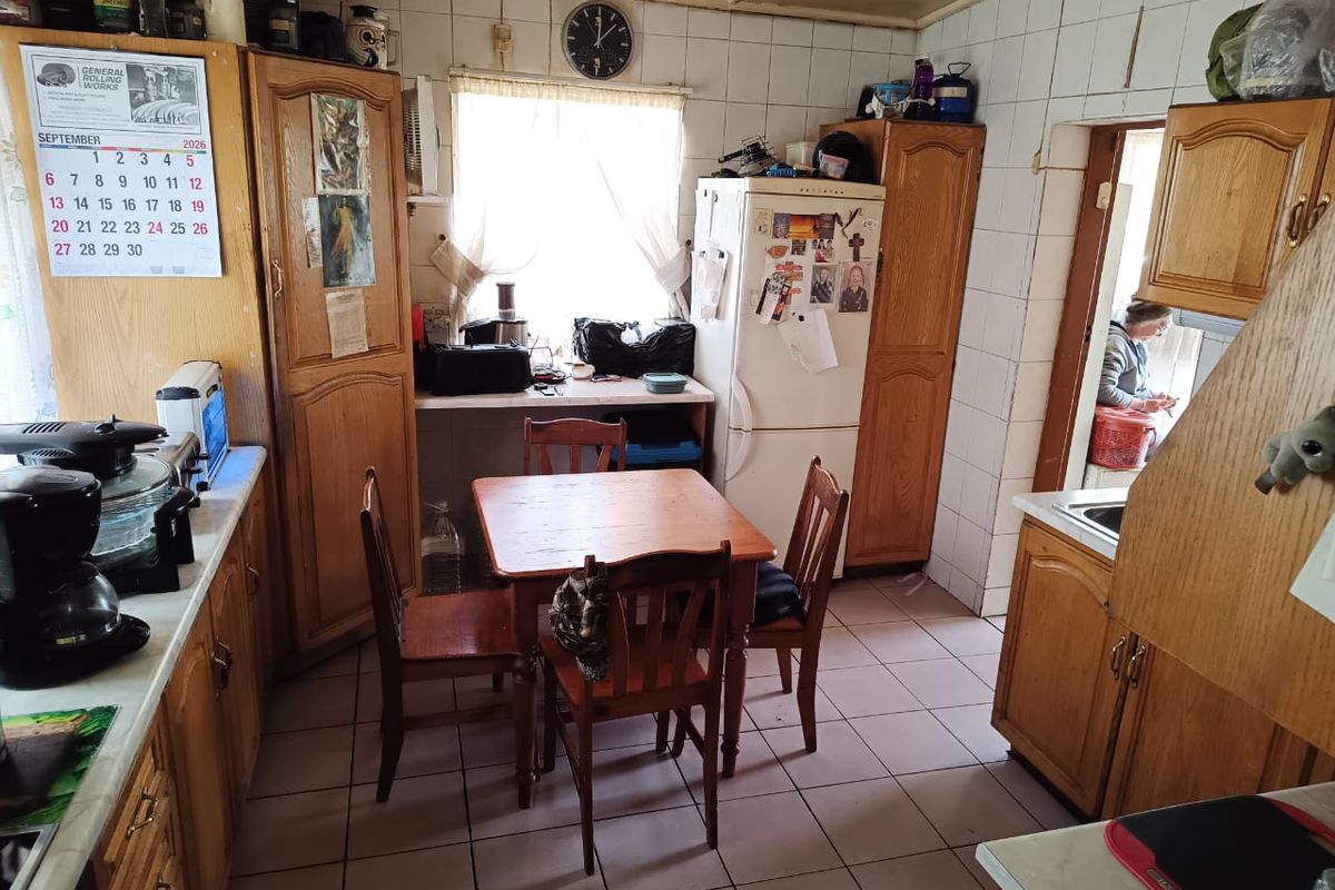 A dated kitchen featuring wooden cabinetry, tiled walls, and tiled flooring, offering a functional layout with potential for modern renovation.