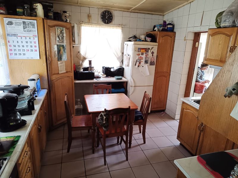 A dated kitchen featuring wooden cabinetry, tiled walls, and tiled flooring, offering a functional layout with potential for modern renovation.