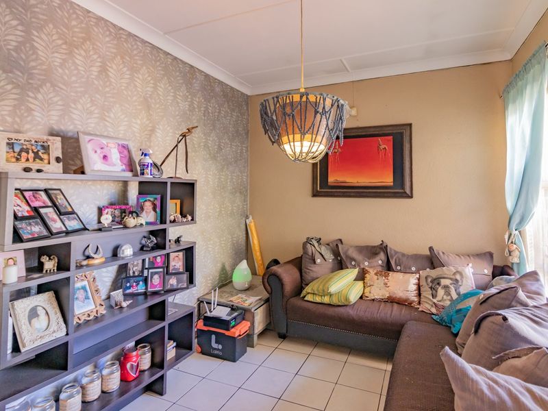 A cozy living room featuring tiled flooring, a decorative pendant light fixture, and a feature wall with patterned wallpaper.