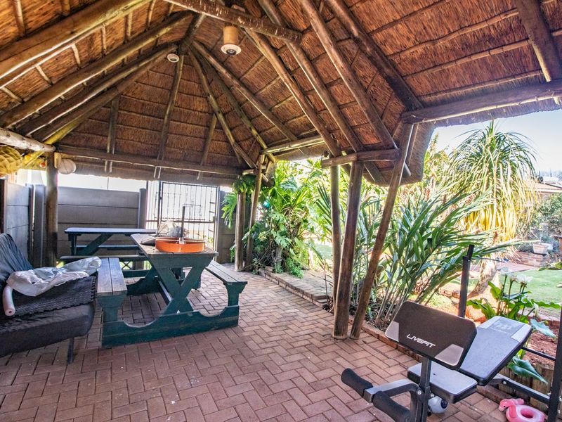 Covered outdoor patio area featuring a traditional thatched roof, timber support structure, and brick paving, overlooking the garden.