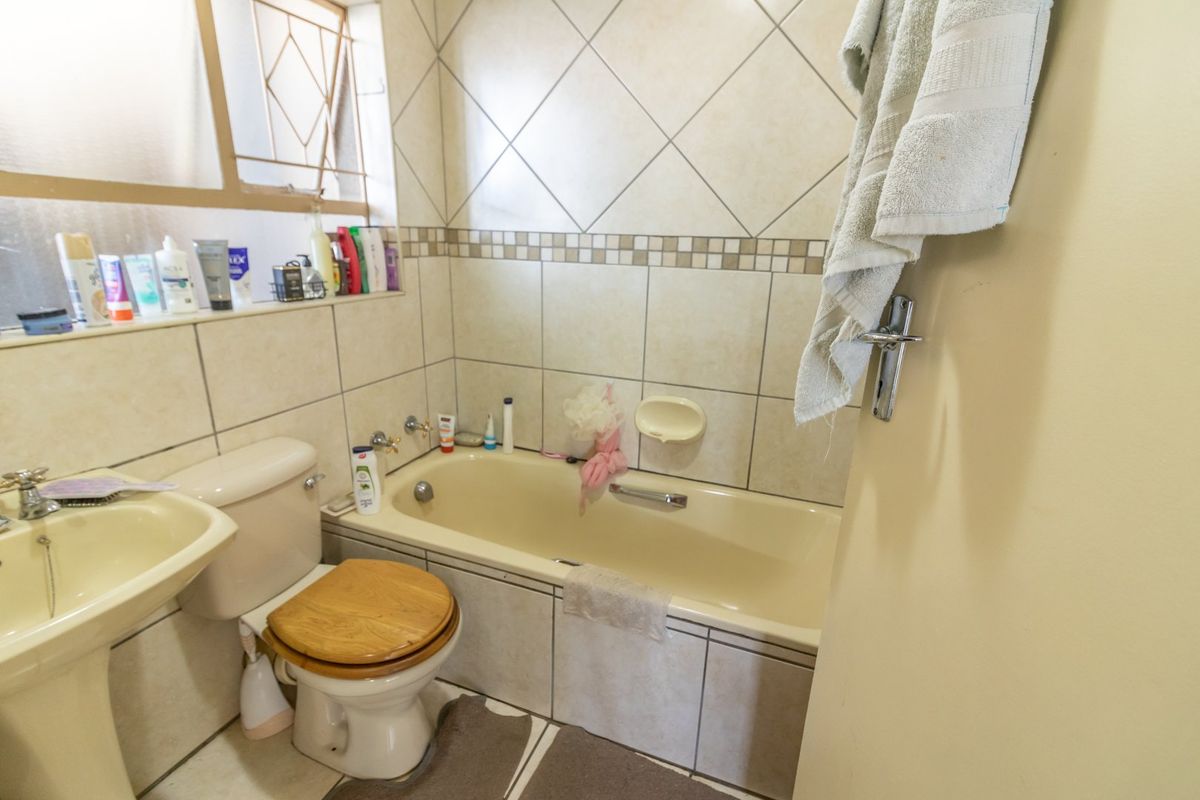 A functional bathroom featuring a pedestal basin, toilet, and built-in bathtub with tiled walls and flooring, offering potential for modern renovation.