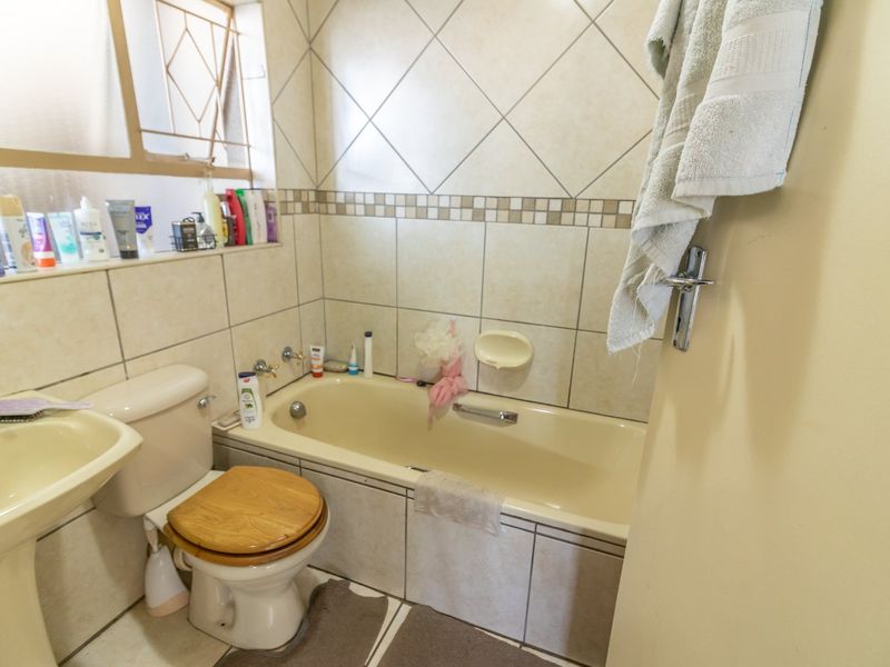 A functional bathroom featuring a pedestal basin, toilet, and built-in bathtub with tiled walls and flooring, offering potential for modern renovation.