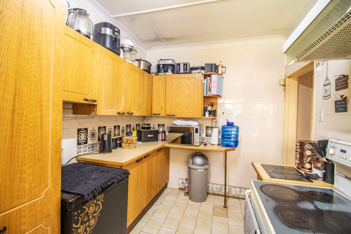 A dated kitchen featuring wood-look laminate cabinetry, tiled splashbacks, and ceramic flooring, equipped with a built-in electric hob and extractor fan.